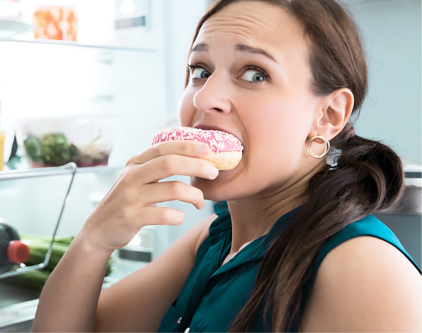 A woman eating a donut near an open refrigerator